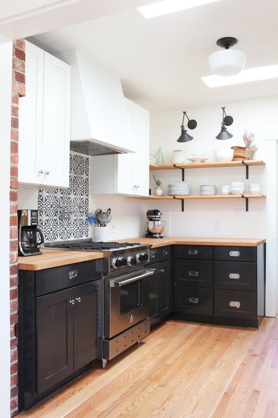 A small and cool black and white L shaped kitchen with open shelves, butcherblock countertops, a printed tile backsplash and skylights