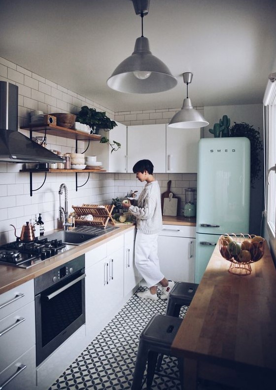 a small and cozy Scandinavian kitchen with white cabinets, butcherblock countertops, a mint fridge and a white tile backsplash
