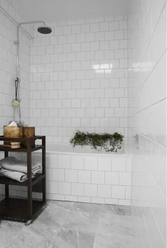 a small bathroom with white and grey marble tiles, adark stained storage unit and some potted plants