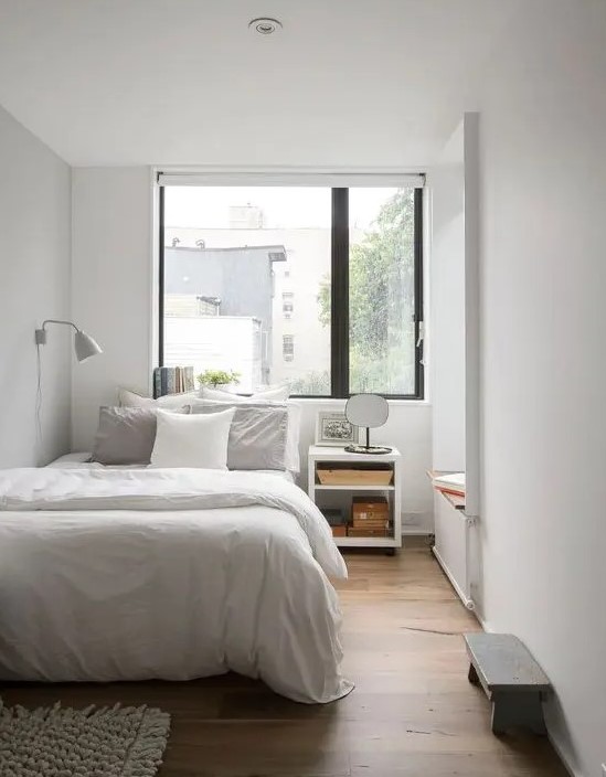 a small bedroom done in neutrals, with a large window over the bed is filled with natural light and looks bigger