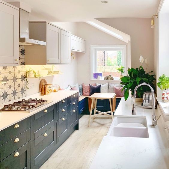 a small galley kitchen with black cabinets, white countertops, star printed tiles and a cozy breakfast zone with pillows