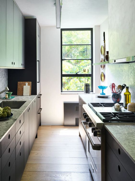 a small galley kitchen with grey stone countertops, open shelves, some appliances and a small window with a black frame