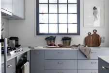 a small grey L-shaped kitchen with white countertops, a black framed window and pendant bulbs