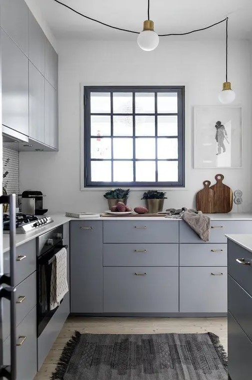 A small grey L shaped kitchen with white countertops, a black framed window and pendant bulbs