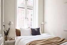 a small neutral Scandinavian bedroom with molding, a bed with neutral bedding, nightstands and wall sconces