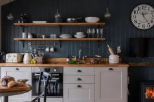 a small pretty kitchen with grey cabinets, a navy accent wall, open shelves, butcherblock countertops and a small hearth