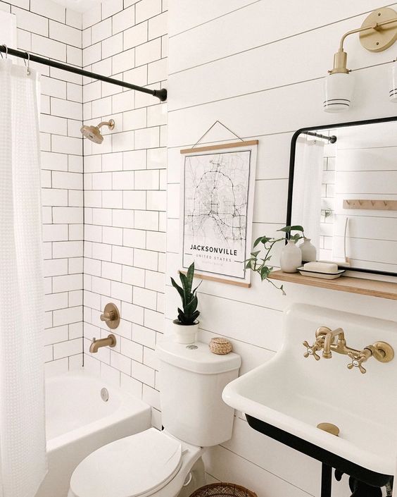a small vintage Nordic bathroom with white subway tiles, beadboard, a vintage sink, brass fixtures and black touches