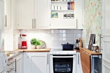 a small white kitchen with a white skinny tile backsplash, a floral wallpaper wall, a folding table and a printed rug