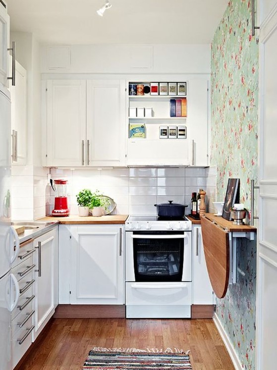 a small white kitchen with a white skinny tile backsplash, a floral wallpaper wall, a folding table and a printed rug