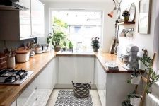 a small white kitchen with butcherblock countertops, potted greenery, a printed rug and pendant lamps
