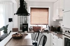 a small white kitchen with dark stained countertops, white tiles on the backsplash, dark pendant lamps and black stools