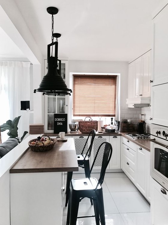 a small white kitchen with dark stained countertops, white tiles on the backsplash, dark pendant lamps and black stools