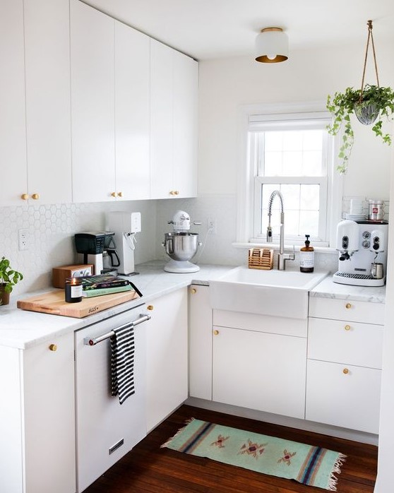 a small white kitchen with penny tiles, with white stone countertops, gold knobs and potted greenery