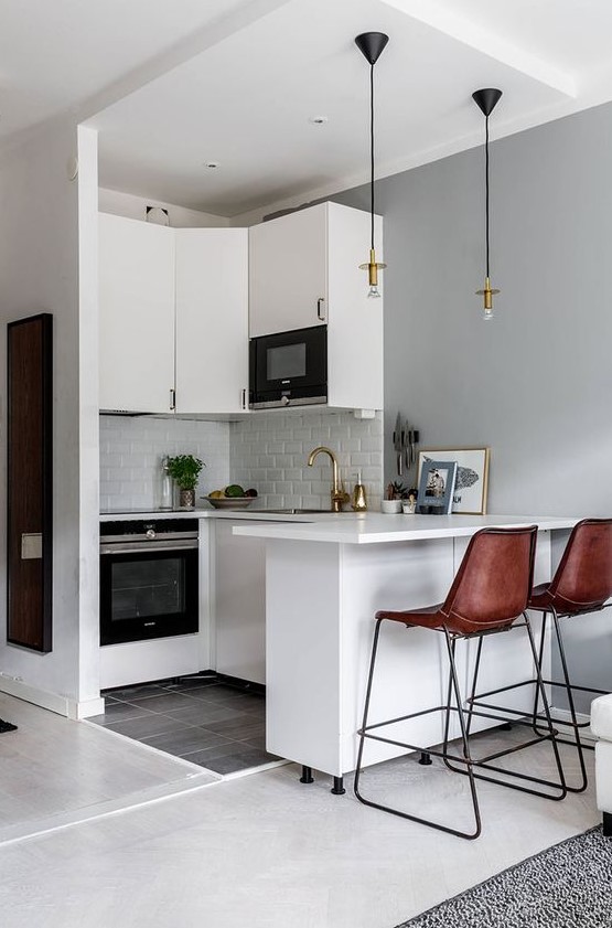 a small white kitchen with white tiles, pendant lamps, brown leather stools and gold touches is chic