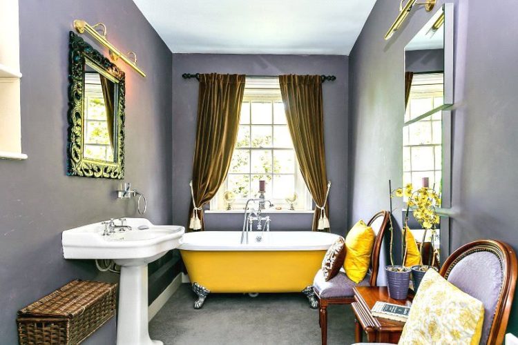 a sophisticated vintage bathroom with grey walls, a yellow clawfoot tub, refined furniture and mustard velvet curtains