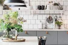 a stylish Scandinavian kitchen with grey cabinets and leather pulls, white square tiles, vintage chairs and pendant lamps