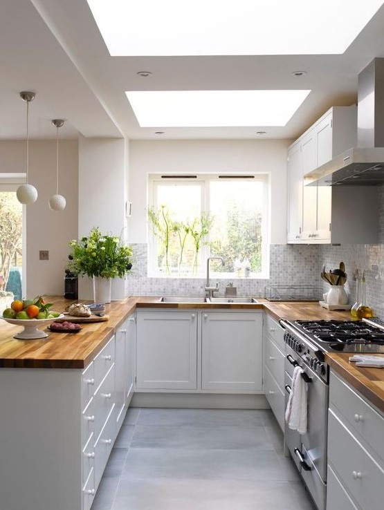 a stylish U shaped kitchen in white, with only lower cabinets and butcherblock countertops, skylights and pendant sphere lamps