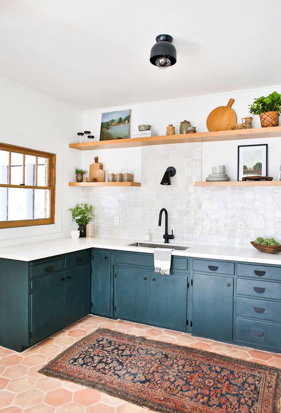 a stylish navy L-shaped kitchen with a white Zellige tile backsplash, open shelves, greenery and black fixtures