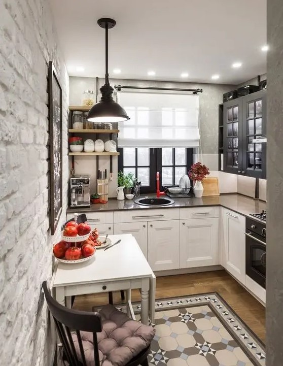 A tiny L shaped kitchen with two tone cabinets, dark countertops and a black pendant lamp plus patterned tiles