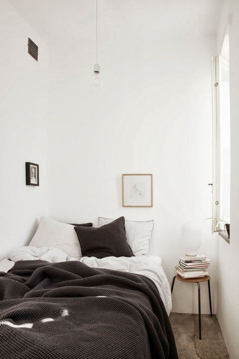 a tiny Nordic bedroom with a bed and black and white bedding, a stool with books and some art is lovely