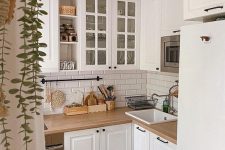 a tiny white L-shaped kitchen with a subway tile backsplasj, butcherblock countertops, a modern chandelier and greenery