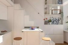 a tiny white kitchen partly built into the staircase, with a retracting table is a smart solution if you face lace of space