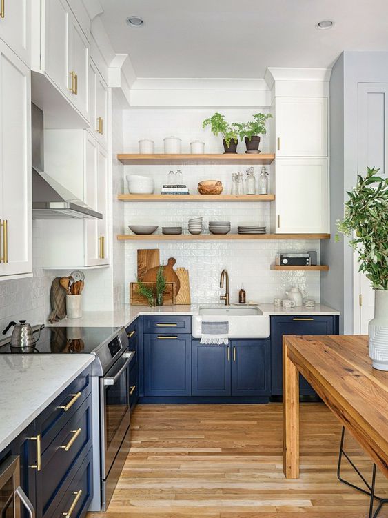 a two-tone farmhouse kitchen with open shelves, white countertops and a backsplash, a stained table and some greenery