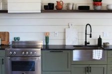 a vintage boho green one wall kitchen with black countertops, a white beadboard backsplash and a hood, a colorful rug