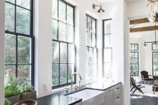 a vintage white one wall kitchen with black countertops, large windows, brass sconces and elegant pendant lamps