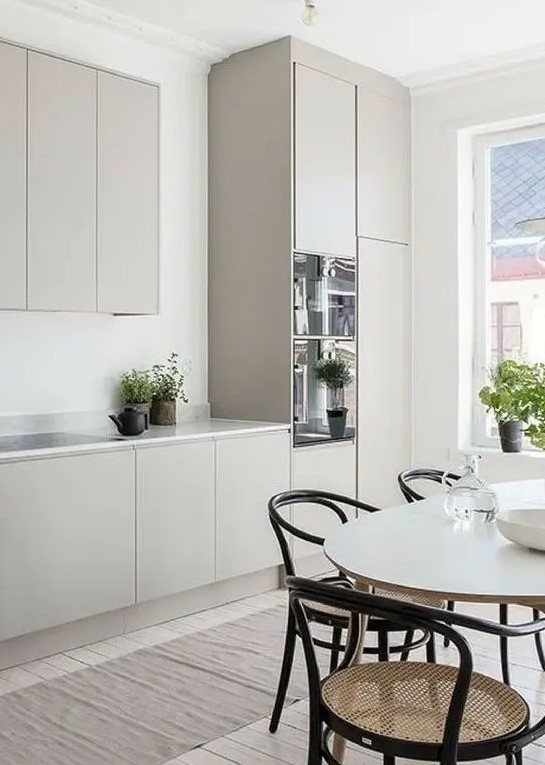 A welcoming Scandinavian kitchen with an oval table, plain grey cabinets, a white marble countertop, and retro rattan chairs. Combine grey cabinets with marble for a fresh look and rattan for a cozy touch.
