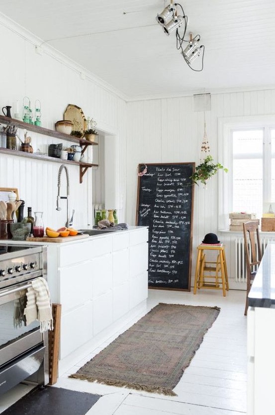 A welcoming and light filled Nordic kitchen with shiplap walls, a white floor, a chalkboard and sleek cabinets plus lights