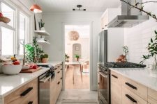 a welcoming light-stained galley kitchen with white countertops and a tile backsplash, with potted greenery and pendant lamps