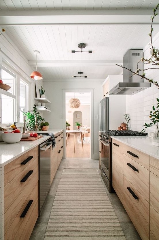 a welcoming light stained galley kitchen with white countertops and a tile backsplash, with potted greenery and pendant lamps