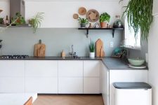 a white L-shaped boho kitchen with a grey backsplash, grey stone countertops, potted greenery is lively and cool