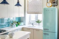 a white L-shaped kitchen with a blue fridge, pendant lamps and patterned tiles on the floor is a pretty and catchy space