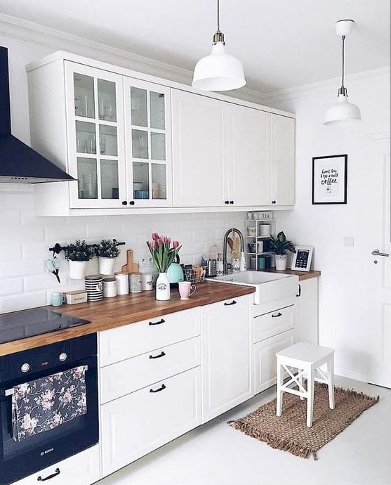 A white Scandi kitchen with vintage inspired cabinets and black hardware, butcherblock countertops and pendant lamps