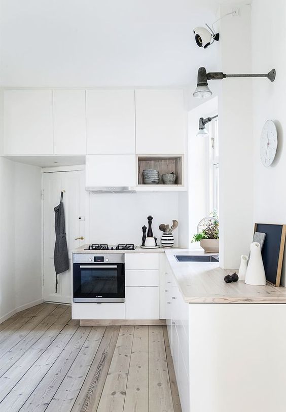 a white Scandinavian L-shaped kitchen with butcherblock countertops, box shelves, black sconces and some decor