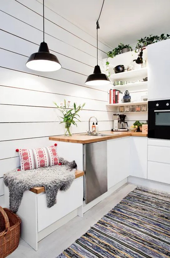 a white Scandinavian kitchen with butcherblock countertops, black pendant lamps and potted greenery