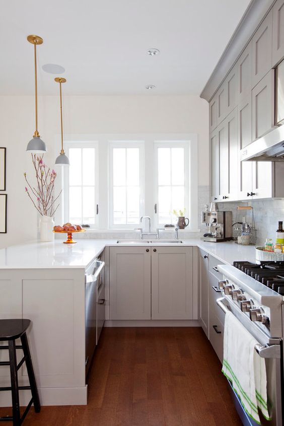 a white U-shaped kitchen with stone countertops, pendant lamps, a black stool and a white tile backsplash