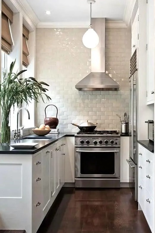 a white farmhouse U-shaped kitchen with a black countertop, a glazed tile backsplash and stainless steel appliances