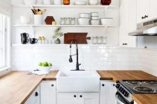 a white farmhouse U-shaped kitchen with butcherblock countertops, black fixtures and open shelves