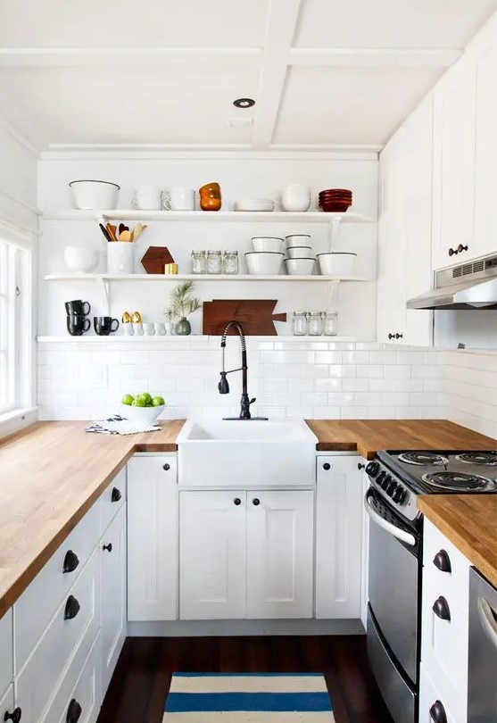 a white farmhouse U-shaped kitchen with butcherblock countertops, black fixtures and open shelves