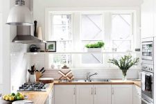 a white farmhouse U-shaped kitchen with butcherblock countertops, built-in appliances, pendant lamps and greenery