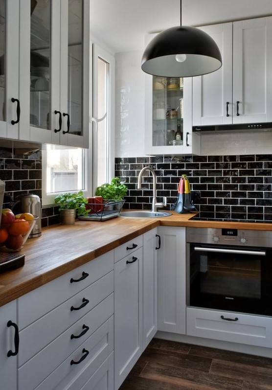a white farmhouse kitchen with a black glazed tiles, butcherblock countertops, black pendant lamps