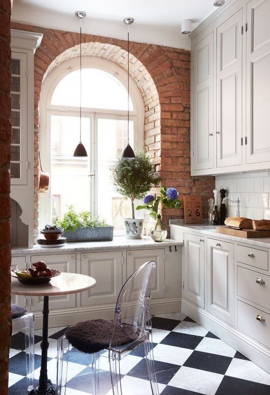 a white farmhouse kitchen with a windowsill and potted plants, a round table, ghost chairs and a white tile backsplash