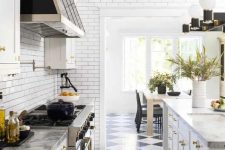 a white farmhouse kitchen with shaker cabinets, stone countertops, black and white tiles, a vintage style hood and cool lamps