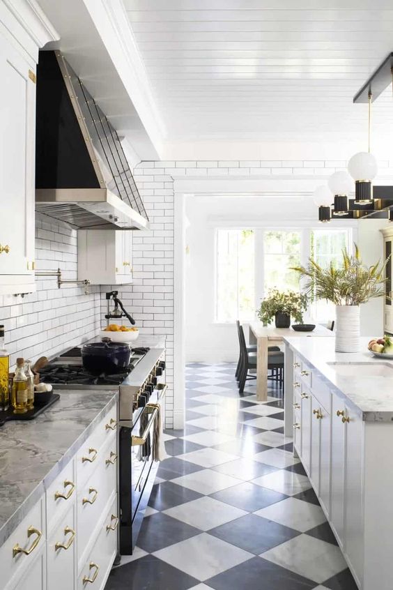 a white farmhouse kitchen with shaker cabinets, stone countertops, black and white tiles, a vintage style hood and cool lamps