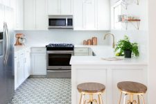 a white farmhouse kitchen with shaker cabinets, stone countertops, open shelves, wooden stools and greenery