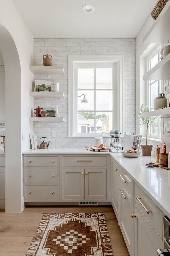 a white farmhouse kitchen with shaker cabinets, white stone countertops, a white marble tile backsplash, open shelves and some decor