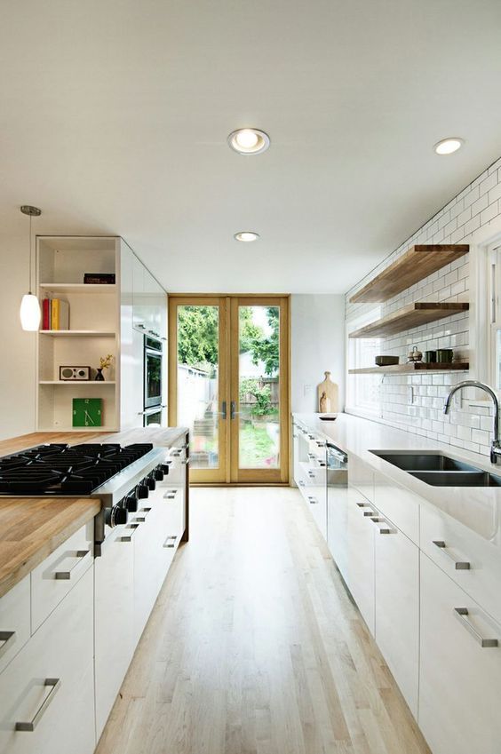 a white galley kitchen with a white subway tile backsplash, open shelves instead of upper cabinets and some lights
